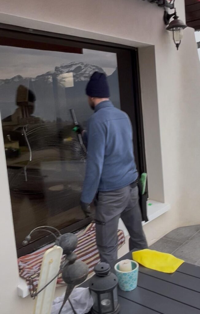 Agent E2A Nettoyage réalisant le lavage d'une baie vitrée avec vue sur les montagnes en Haute-Savoie